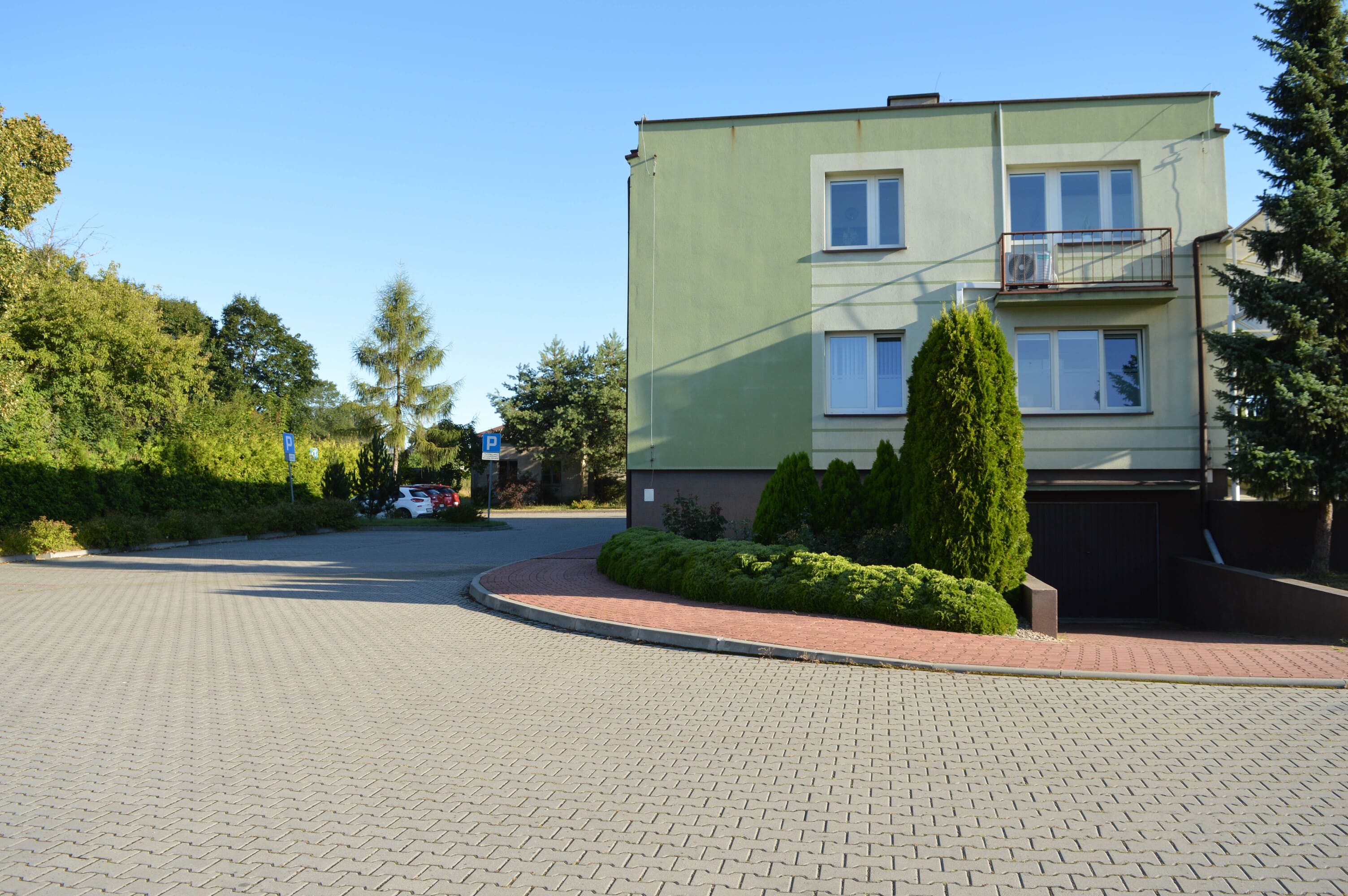 Brukowany podjazd na parking z chodnikiem w tle widoczny budynek przychodni. 